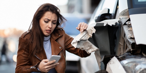 Woman looking at her phone next to damaged car