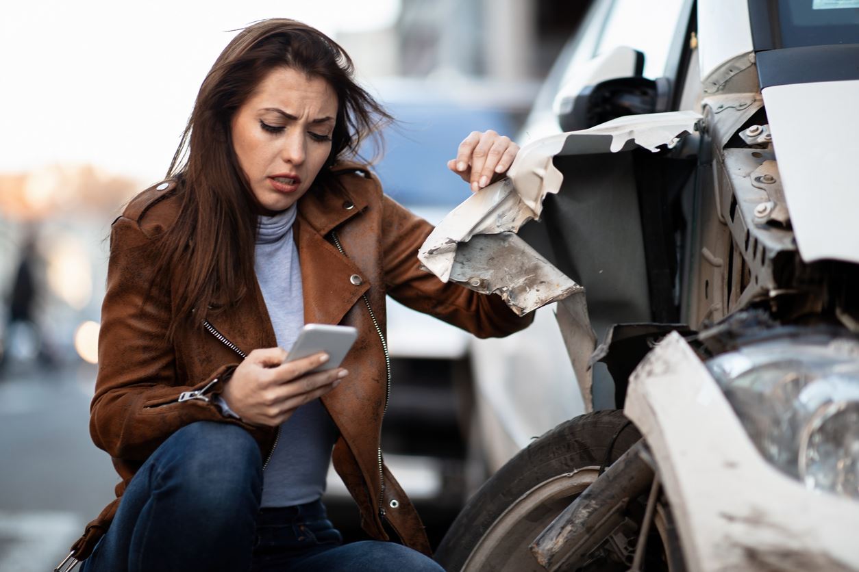 Woman looking at her phone next to damaged car